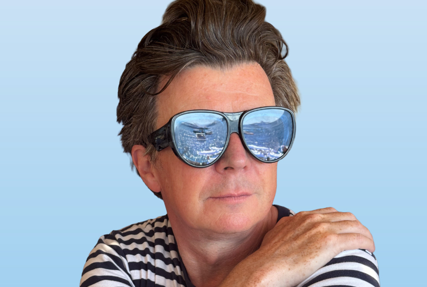 Musician Rick Astley wearing sunglasses which reflect a crowd.